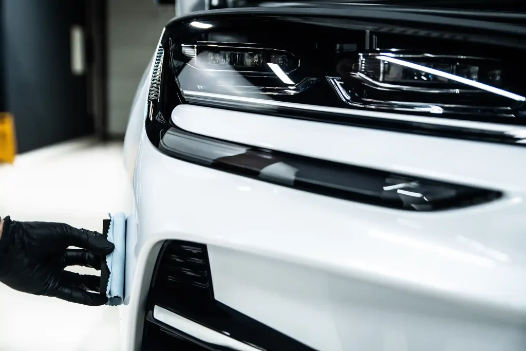 Détaillant appliquant un revêtement en céramique sur un pare-chocs avant de voiture blanche près du phare. Protection Professionnel de la peinture et amélioration du brillant dans le processus de détail automatique.