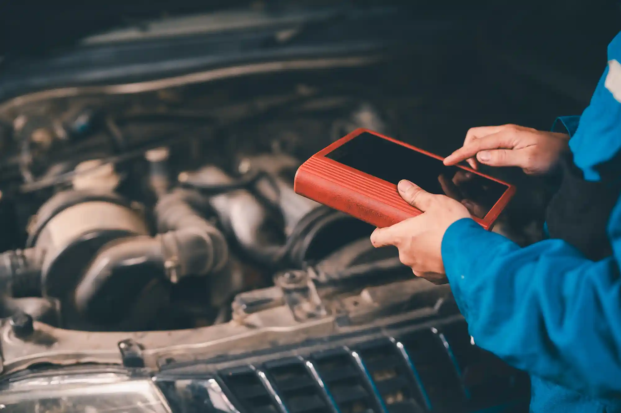 Un mécanicien utilise une tablette de diagnostic pour inspecter un moteur de voiture sous le capot dans un atelier.
